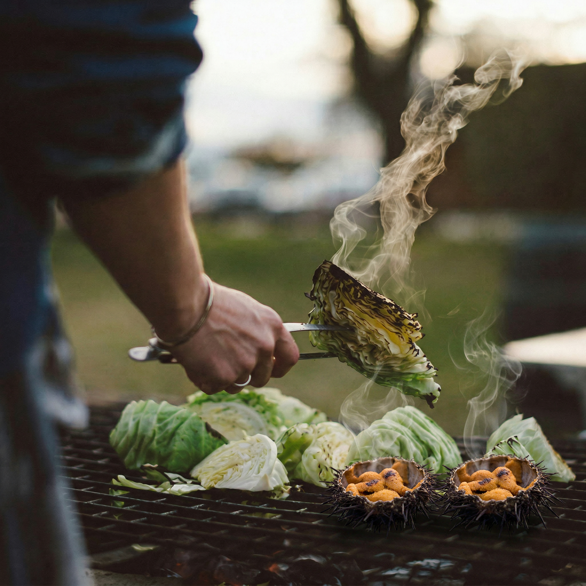uni grilling in the shell alongside charred vegetables over open fire